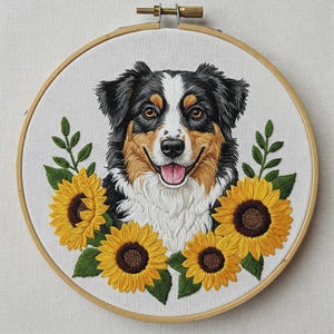Può includere: Un telaio da ricamo contenente un ritratto dettagliato cucito a filo di un cane pastore australiano con pelo nero, bianco e marrone chiaro. Il cane è raffigurato con la bocca aperta e la lingua rosa, circondato da quattro girasoli gialli vivaci.