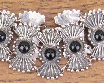 May include: A silver chain bracelet with black onyx stones and a decorative fan-shaped design.