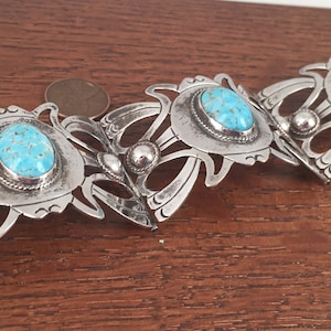 May include: A silver-toned bracelet featuring three oval turquoise stones set in ornate, stylized settings. The bracelet has an Art Nouveau design with intricate, flowing lines and decorative elements. The turquoise stones have a speckled appearance.