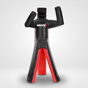 May include: A black and red grappling dummy with arms raised in a defensive position. The chest features the white and red text MOXEL SPORTS. This training equipment is constructed from durable material with a humanoid shape and wide stance.