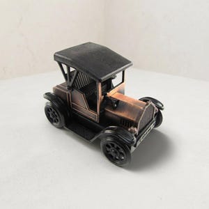 May include: A miniature vintage-style automobile figurine crafted from metal with a dark copper and black finish. The model features a prominent black roof, detailed wheels, a front grille, and a small horn mounted on the side of the hood.