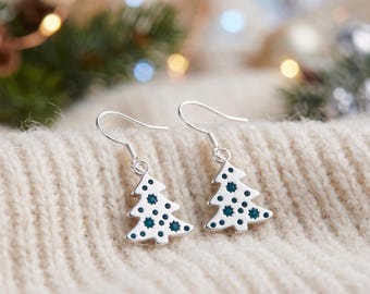 May include: A pair of silver-toned drop earrings featuring a Christmas tree shape. Each tree charm is decorated with small, dark teal circular accents and hangs from a simple silver-toned hook wire for pierced ears.