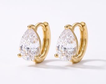 May include: A pair of gold hoop earrings featuring a teardrop-shaped clear gemstone set in the center. The earrings have a polished gold finish and a hinged closure mechanism, showcasing a classic design with a faceted stone that reflects light.