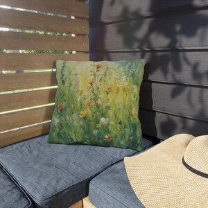 May include: A square throw pillow featuring a vibrant, painterly print of a lush meadow filled with wildflowers in shades of yellow, green, orange, and blue. The design depicts a dense field of grass and various floral blooms with soft brushstrokes.