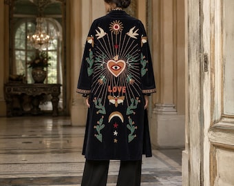 May include: A long, black velvet duster coat featuring intricate, colorful embroidery on the back. The design includes a central heart with an eye, the word LOVE, a moth, sun, moon, stars, birds, and cactus motifs in shades of red, gold, and green.
