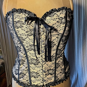 May include: A black and beige lace corset with a black satin ribbon tie and a row of black buttons down the front.