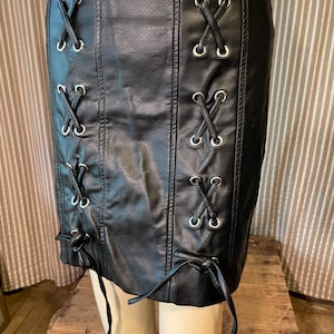 May include: Black faux leather mini skirt with silver grommets and laces that tie at the bottom.