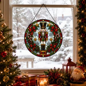May include: A circular stained glass suncatcher featuring a nutcracker in a red and green uniform, surrounded by holly, red bows, and white snowflakes. The piece is framed by a dark border and hangs from a black metal chain against a window.