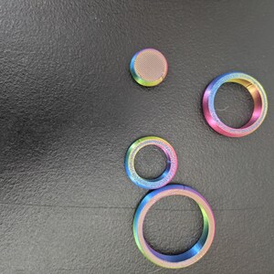 Peut inclure: Un ensemble de quatre composants m&eacute;talliques iridescents avec une finition d&eacute;grad&eacute;e arc-en-ciel. Le lot comprend un disque circulaire plein &agrave; surface textur&eacute;e et trois anneaux circulaires ouverts de diam&egrave;tres vari&eacute;s, tous &agrave; l'&eacute;clat m&eacute;tallique.