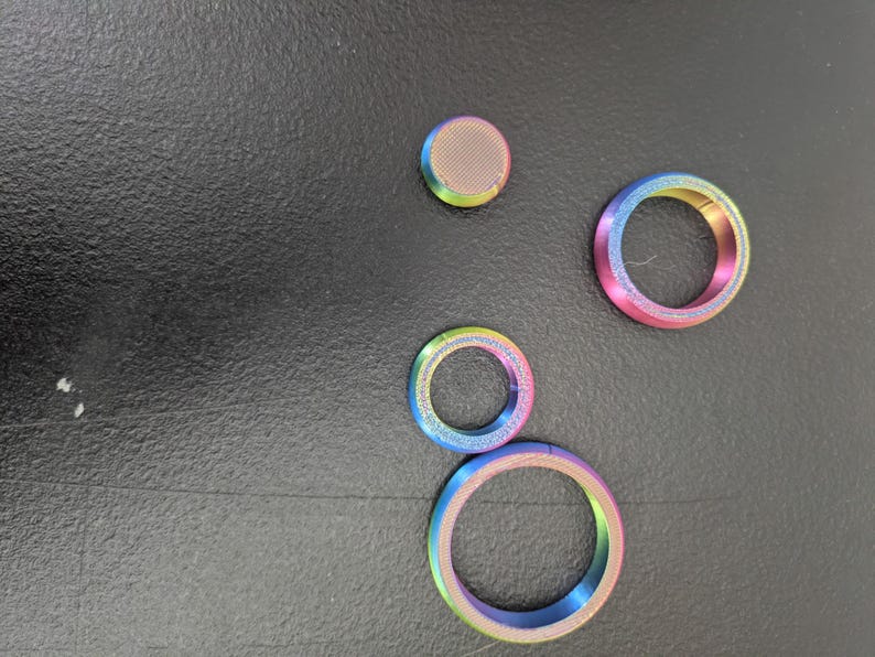 Peut inclure: Un ensemble de quatre composants m&eacute;talliques iridescents avec une finition d&eacute;grad&eacute;e arc-en-ciel. Le lot comprend un disque circulaire plein &agrave; surface textur&eacute;e et trois anneaux circulaires ouverts de diam&egrave;tres vari&eacute;s, tous &agrave; l'&eacute;clat m&eacute;tallique.