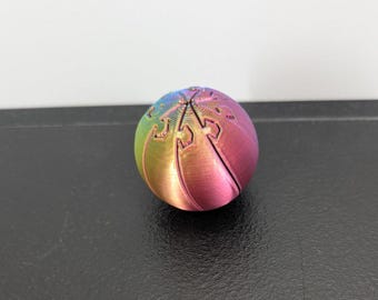 Peut inclure: Un objet sphérique avec une finition arc-en-ciel dégradée passant du bleu au vert, au jaune et au rose. La surface présente une série de segments incurvés et imbriqués qui se rejoignent au sommet, créant un motif distinct de fines lignes verticales.