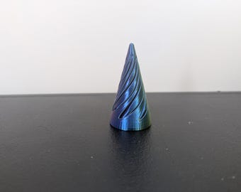 Peut inclure: Un objet conique avec une texture rainurée en spirale. La surface présente une finition métallique irisée qui change de couleur entre le bleu profond, le violet et des nuances de vert, créant un aspect dynamique sur toute la forme effilée.