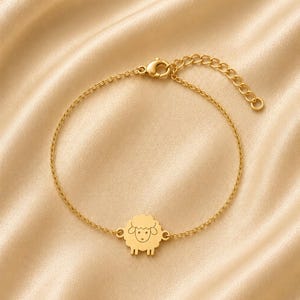 Puede incluir: Una pulsera de cadena en tono dorado con un dije central en forma de oveja estilizada con un rostro grabado sencillo. La pulsera incluye una cadena de eslabones finos y un cierre de mosquetón con una cadena de extensión ajustable para el ajuste.