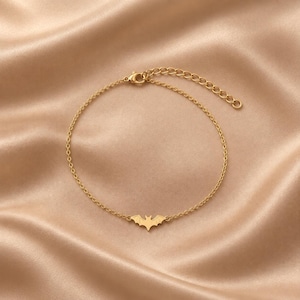 Op de afbeelding: Een enkelbandje van goudkleurige metalen ketting met een kleine, platte vleermuisvormige bedel in het midden van de fijne schakelketting. Het sieraad is voorzien van een karabijnsluiting en een verstelbare verlengketting met ronde schakels.