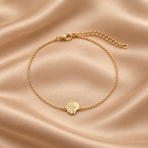 Könnte beinhalten: Ein goldfarbenes Kettenarmband mit einem zentralen Anhänger in Herzform, wobei eine Hälfte ein Gehirn und die andere eine Glühbirne darstellt. Das Armband besteht aus einer feinen Gliederkette und einem Karabinerverschluss für sicheren Halt.