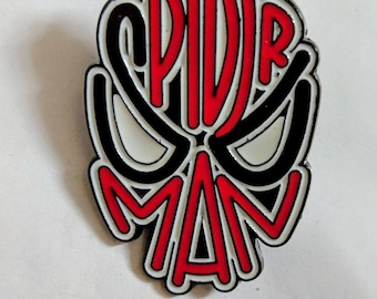 Könnte beinhalten: Eine Metall-Emaille-Anstecknadel in Form einer stilisierten Maske mit dem in das Design integrierten Text SPIDER MAN. Die Anstecknadel zeigt kräftige rote Buchstaben, schwarze Umrisse und weiße Akzente, die eine grafische Darstellung eines Gesichts bilden.