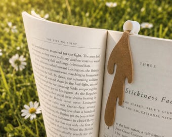 May include: A bookmark shaped like a spilled cup of coffee, featuring a white cylindrical cup top and a long, brown, fluid-like drip extending down the page of an open book titled The Tipping Point, with visible printed text on the pages.