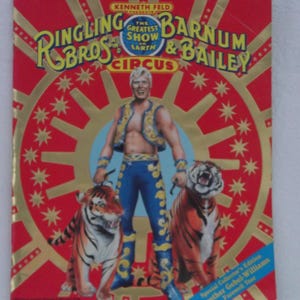 May include: A red, white, and gold circus poster featuring a man in a blue and white costume standing between two tigers. The poster reads "Ringling Bros. and Barnum & Bailey Circus, The Greatest Show on Earth".
