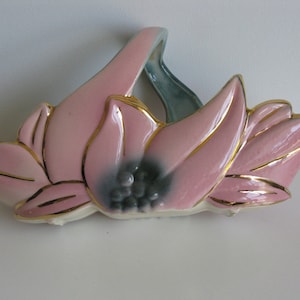 May include: A pink and green ceramic wall planter shaped like a flower with gold accents. The planter has a handle and is designed to hold a small plant.