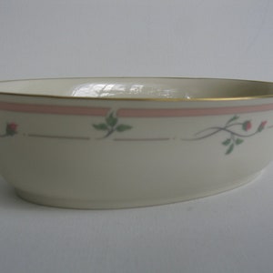May include: A white oval serving bowl with a gold rim and a pink and green floral design.