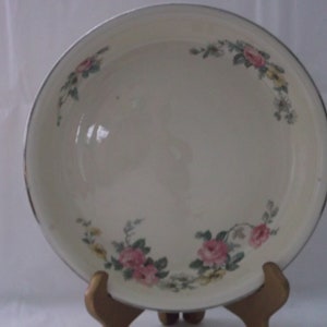 May include: A white ceramic serving bowl with a floral design. The bowl has a silver rim and features pink and yellow flowers with green leaves.