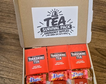 May include: A cardboard gift box containing three red Yorkshire Tea bags, two small Daim chocolate bars, and three Lotus Biscoff biscuit packets. The inside lid features a white label with the text TEA SURVIVAL PACK EMERGENCY SUPPLIES.