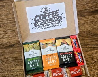 May include: A cardboard gift box containing three Taylors of Harrogate coffee bag packets in green, orange, and black, two red Daim chocolate bars, and three Lotus Biscoff biscuit packs. The lid features a label reading Coffee Survival Pack.