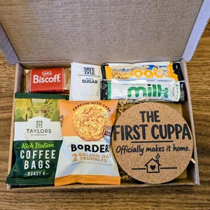 May include: A cardboard gift box containing a Biscoff biscuit, a Tate & Lyle sugar packet, two small milk cartons, a pack of Taylors of Harrogate coffee bags, a Border Golden Oat Crumbles biscuit pack, and a round cork coaster with the text THE FIRST CUPPA Officially makes it home.
