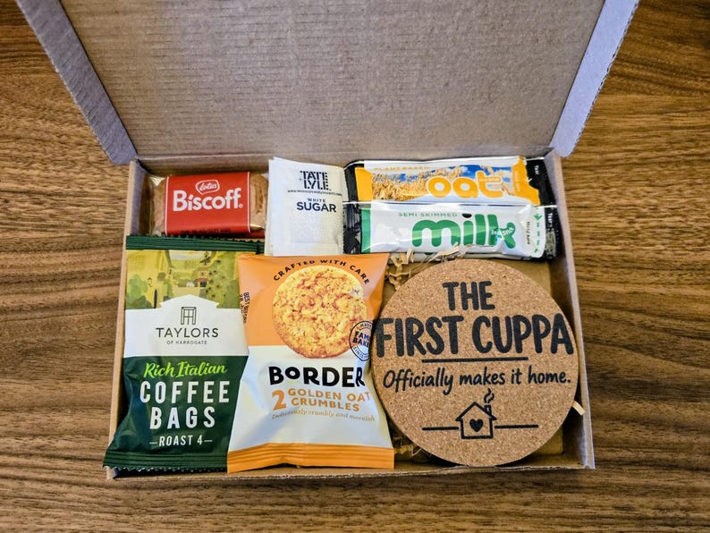 May include: A cardboard gift box containing a Biscoff biscuit, a Tate & Lyle sugar packet, two small milk cartons, a pack of Taylors of Harrogate coffee bags, a Border Golden Oat Crumbles biscuit pack, and a round cork coaster with the text THE FIRST CUPPA Officially makes it home.