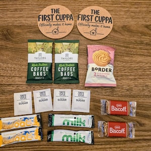 May include: Two round cork coasters with the text THE FIRST CUPPA Officially makes it home, two Taylors Rich Italian coffee bags, a Border Viennese Whirls pack, four Tate & Lyle sugar sachets, two Oat milk sticks, two semi-skimmed milk sticks, and two Biscoff biscuits.