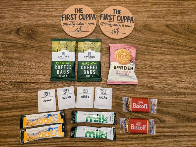 May include: Two round cork coasters with the text THE FIRST CUPPA Officially makes it home, two Taylors Rich Italian coffee bags, a Border Viennese Whirls pack, four Tate & Lyle sugar sachets, two Oat milk sticks, two semi-skimmed milk sticks, and two Biscoff biscuits.