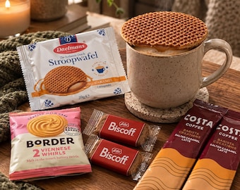 May include: A speckled ceramic mug filled with a hot beverage topped with a round, grid-patterned Daelmans stroopwafel. Beside it are a Daelmans stroopwafel package, a Border Viennese Whirls packet, two Biscoff biscuit packs, and two Costa Coffee Salted Caramel Latte sachets.