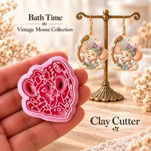 Könnte beinhalten: Ein rosa Kunststoff-Ausstecher mit einer Maus in einer Badewanne mit Duschkopf, neben einem Paar passender Ohrhänger auf einem goldenen Ständer. Der Text lautet Bath Time Vintage Mouse Collection und Clay Cutter.