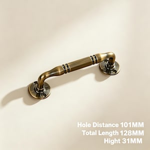 Può includere: Una maniglia per mobili con finitura in ottone anticato, dotata di un centro cilindrico e due piastre di montaggio circolari. La maniglia presenta una distanza tra i fori di 101mm, una lunghezza totale di 128mm e un'altezza di 31mm, come indicato.