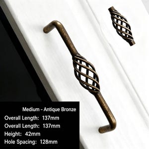May include: An antique bronze cabinet handle featuring a central cage-like twisted metal design. The handle has an overall length of 137mm, a height of 42mm, and a hole spacing of 128mm. A smaller matching handle piece is visible in the upper right corner.
