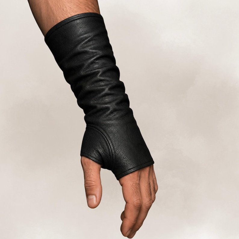 May include: A black fingerless glove made of textured material that extends from the knuckles up to the forearm. The glove features a thumb hole and a fitted design with subtle vertical folds along the length of the arm, covering the wrist.