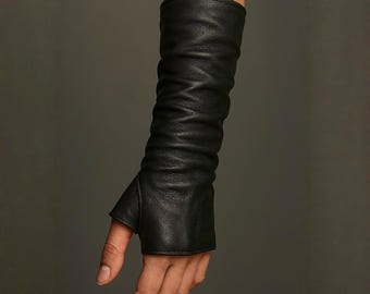 May include: A long black leather glove that extends past the wrist and up the forearm. The glove features a thumb hole and a fingerless design, with a soft, textured surface that creates natural folds and creases along the length of the arm.