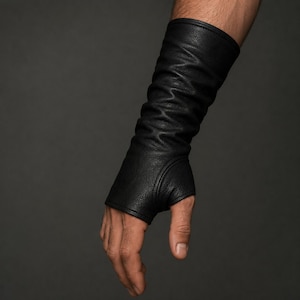 May include: A black, long, fingerless glove made of a textured material that extends from the knuckles up to the forearm. The glove features a fitted design with a dedicated opening for the thumb and a smooth, stitched hem at the top edge.
