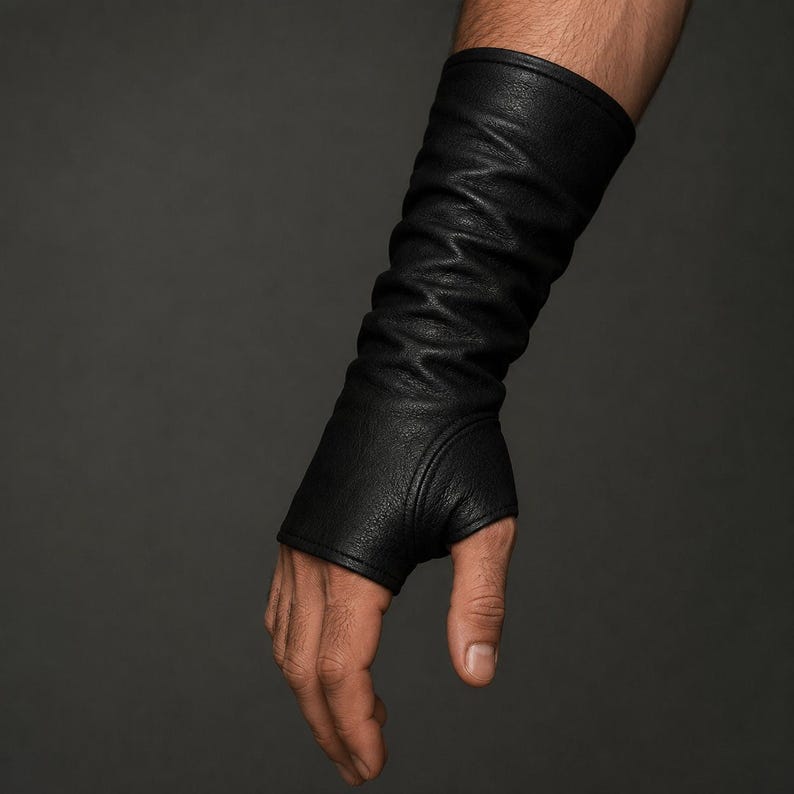 May include: A black, long, fingerless glove made of a textured material that extends from the knuckles up to the forearm. The glove features a fitted design with a dedicated opening for the thumb and a smooth, stitched hem at the top edge.