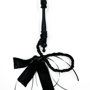 Könnte beinhalten: Schwarzer Zauberstab mit Perlenakzenten und einer Schleife aus Satinband. Der Zauberstab hat einen langen, schlanken Griff und eine dekorative Schleife mit Perlenkanten. Das Design ist komplett schwarz und erzeugt eine elegante Ästhetik.