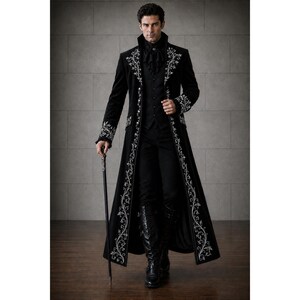 May include: A black long coat featuring intricate white floral embroidery along the lapels, cuffs, and front edges. The coat is worn over a black vest, a black shirt with a ruffled collar, black trousers, and black boots, accompanied by a black cane.