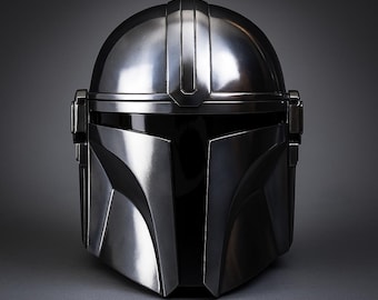 Könnte beinhalten: Ein metallisch silberner Helm mit glatter, polierter Oberfläche und einem dunklen, horizontalen Visier. Der Helm verfügt über einen Mittelsteg, der von oben bis zum Nasenbereich verläuft, sowie kantige Wangenplatten und seitliche Kappen.
