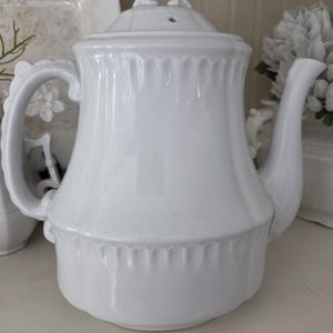May include: A white ceramic mug with a black handle and the text "But First, Coffee" in a bold, black font. The mug is sitting on a wooden surface. The mug is approximately 4 inches tall.