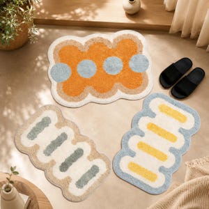 May include: Three tufted rugs with irregular, wavy edges. One rug features a large orange central shape with light blue circles. Another rug displays sage green bars on a cream background. The third rug has yellow bars on a light blue border.