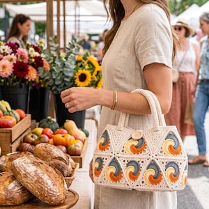 Könnte beinhalten: Eine cremefarbene Häkeltasche mit einem Muster aus dreieckigen Motiven. Jedes Dreieck enthält ein Spiraldesign in Orange-, Gelb- und Dunkelgrautönen. Die Tasche verfügt über zwei Tragegriffe und einen einzelnen Holzknopfverschluss in der Mitte.