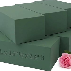 May include: A stack of rectangular dark green floral foam blocks with the text 7.8" L x 3.5" W x 2.4" H embossed on the front surface, accompanied by a single pink rose with green leaves positioned at the bottom right corner of the arrangement.