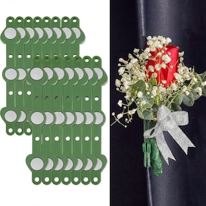 May include: A set of green plastic magnetic corsage holders with circular silver magnets, shown alongside a floral arrangement featuring a red rose, white baby's breath, and eucalyptus leaves, accented with a shimmering silver ribbon.
