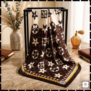 May include: A square scarf featuring a dark brown and cream colour palette with a repeating pattern of stylised flowers and geometric shapes. The border includes a yellow and white decorative trim with small repeating symbols along the edge.
