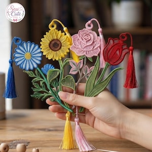以下が含まれることがあります： 刺繍レースで作られた4つの花のしおり。青いデイジー、黄色いヒマワリ、ピンクのバラ、赤いチューリップがデザインされています。各しおりには緑の茎と葉、上部に円形のループ、そして色を合わせたタッセルが付いています。