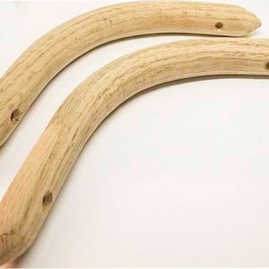 May include: Two curved wooden handles with a light brown finish. Each handle has a hole drilled near the center and at one end. The handles are likely for a bag or purse.